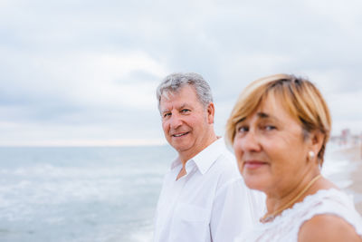 Portrait of smiling senior couple standing at beach 