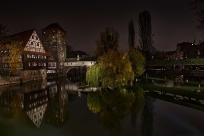 Illuminated buildings by river against sky at night