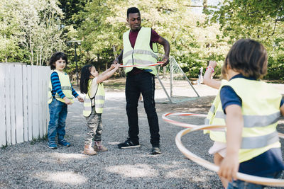 Male teacher and students playing with plastic hoops in playground