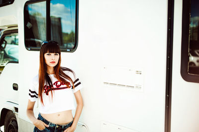 Portrait of young woman standing by camper trailer