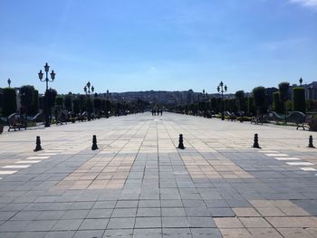 People on footpath in city against blue sky