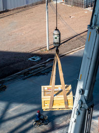 The crane carrying a transportation wooden box and a worker riding a bicycle on the ground