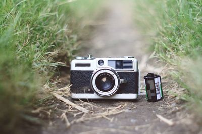 Close-up of old-fashioned camera and reel on dirt amidst grass