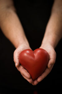 Close-up of hand holding heart shape against black background