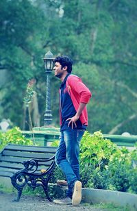 Side view of young man looking away while standing by bench