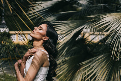 Elegant sensual woman brunette bride in a silk wedding dress posing among palm trees in the park