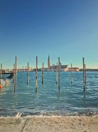 Wooden posts in sea against clear blue sky