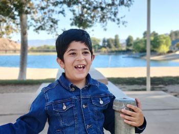 Portrait of smiling boy holding sunglasses against trees