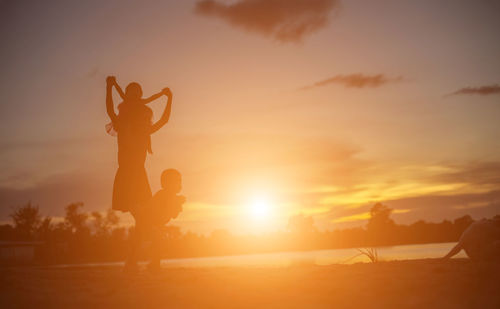 Silhouette people standing on field against sky during sunset