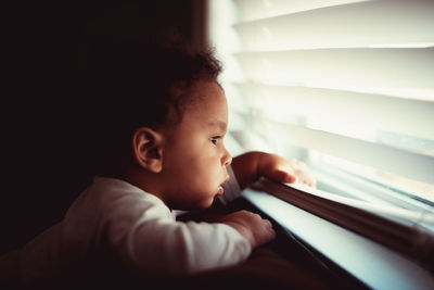 Portrait of boy looking through window at home