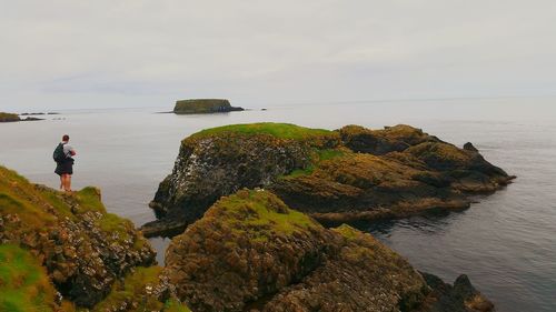 Rear view of man standing on cliff by sea against sky