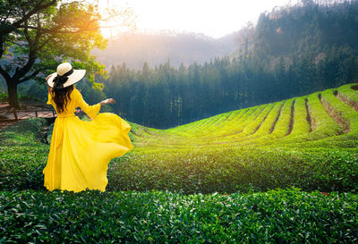 Rear view of woman in yellow dress standing on field