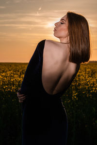 Midsection of woman standing on field against sky during sunset