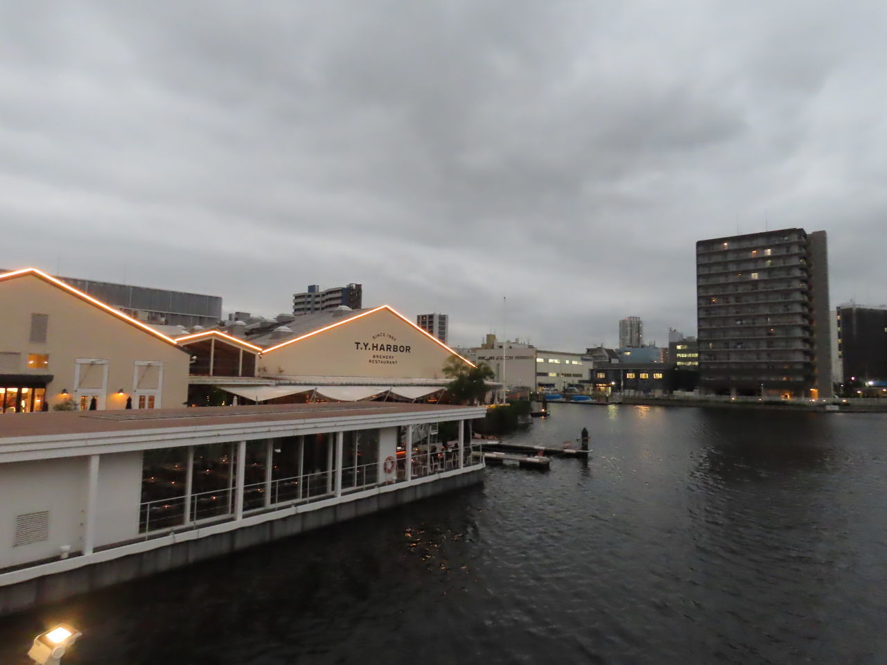 ILLUMINATED BUILDINGS BY RIVER AGAINST SKY IN CITY AT DUSK