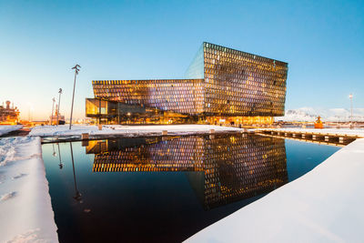 Reflection of illuminated buildings in city against clear blue sky