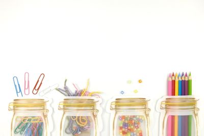 High angle view of multi colored objects spilling from glass jars on white background