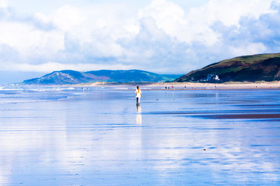 Rear view of woman walking at shore against sky