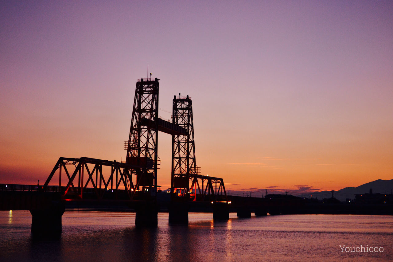 sunset, built structure, architecture, orange color, silhouette, connection, copy space, water, clear sky, bridge - man made structure, engineering, sky, industry, dusk, crane - construction machinery, waterfront, river, development, sea, building exterior