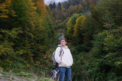 Young man standing by trees in forest