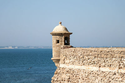 Lighthouse by sea against clear blue sky