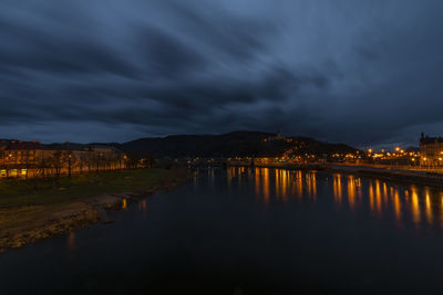 Illuminated city by river against sky at night