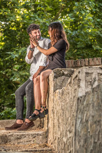Smiling couple touching hands while siting on wall outdoors