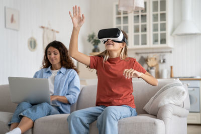 Young woman using phone while sitting on sofa at home