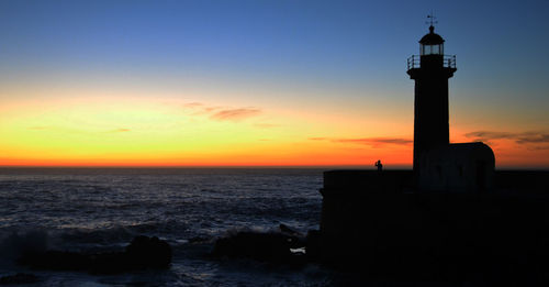 Silhouette of lighthouse at seaside during sunset