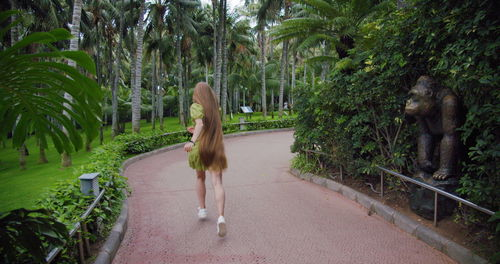 Woman running in the park. tropical palm tree garden. short green dress. very long hair.