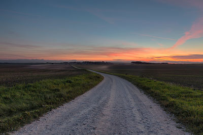 Road amidst agricultural field against sky during sunset