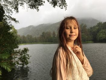 Portrait of girl standing by lake against sky