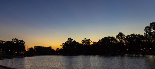 Silhouette trees by river against sky at sunset