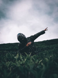 Person with arms raised on field against sky