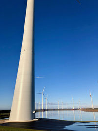 View of windturbines at lake against clear blue sky