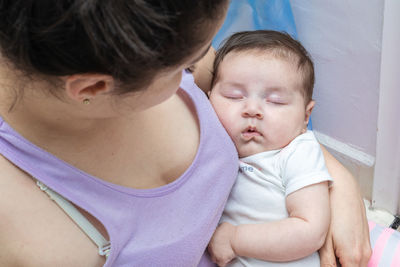 Latin mother looking at her baby as she sleeps tenderly in her arms after breastfeeding