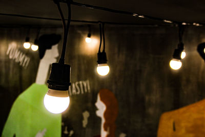 Close-up of illuminated light bulbs hanging by wall