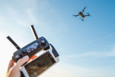 Cropped hand of person operating drone against sky