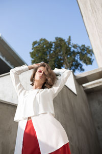 Low angle portrait of young woman standing against clear sky