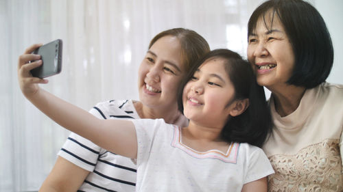 Smiling girl taking selfie with mother and grandmother at home