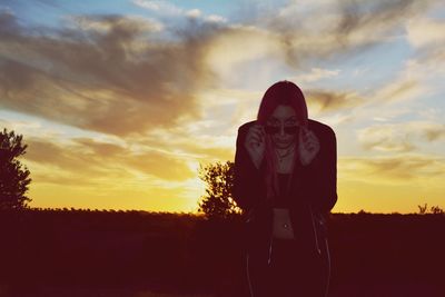 Portrait of woman standing on field against sky during sunset