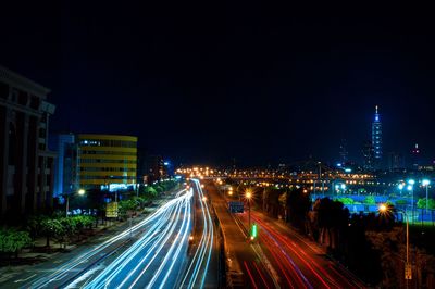 Light trails on road amidst buildings against sky at night