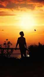 Silhouette man standing by tree against orange sky