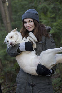 Portrait of smiling woman carrying dog while standing against trees