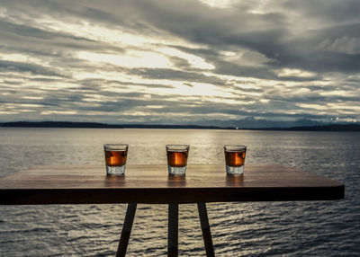 Shots of whiskey on seaside table under dramatic sky.