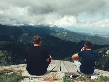 Rear view of men sitting on mountain against sky