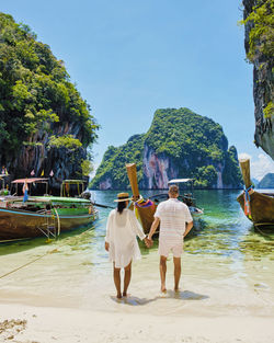 Rear view of couple walking at beach against clear sky