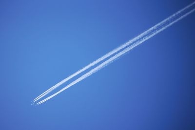 Low angle view of vapor trails in blue sky