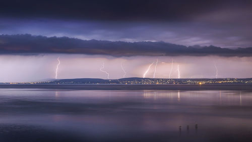 Scenic view of beach against lighting at dusk