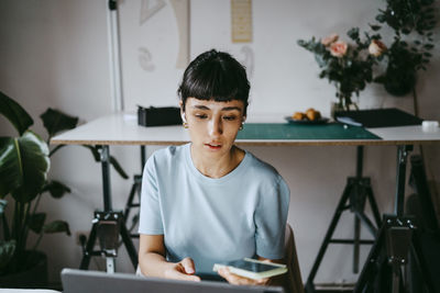 Young female freelancer talking through smart phone while using laptop at home