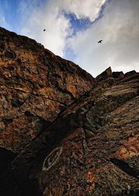 Low angle view of birds flying over mountain against sky